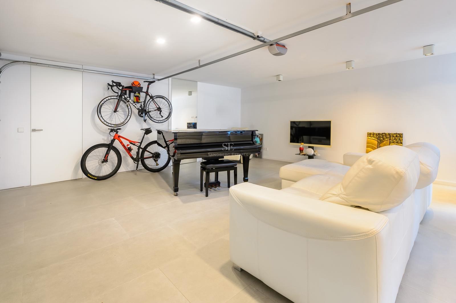 Sala moderna con un piano de cola negro, bicicletas montadas en la pared y un sofá de cuero blanco sobre suelo gris.