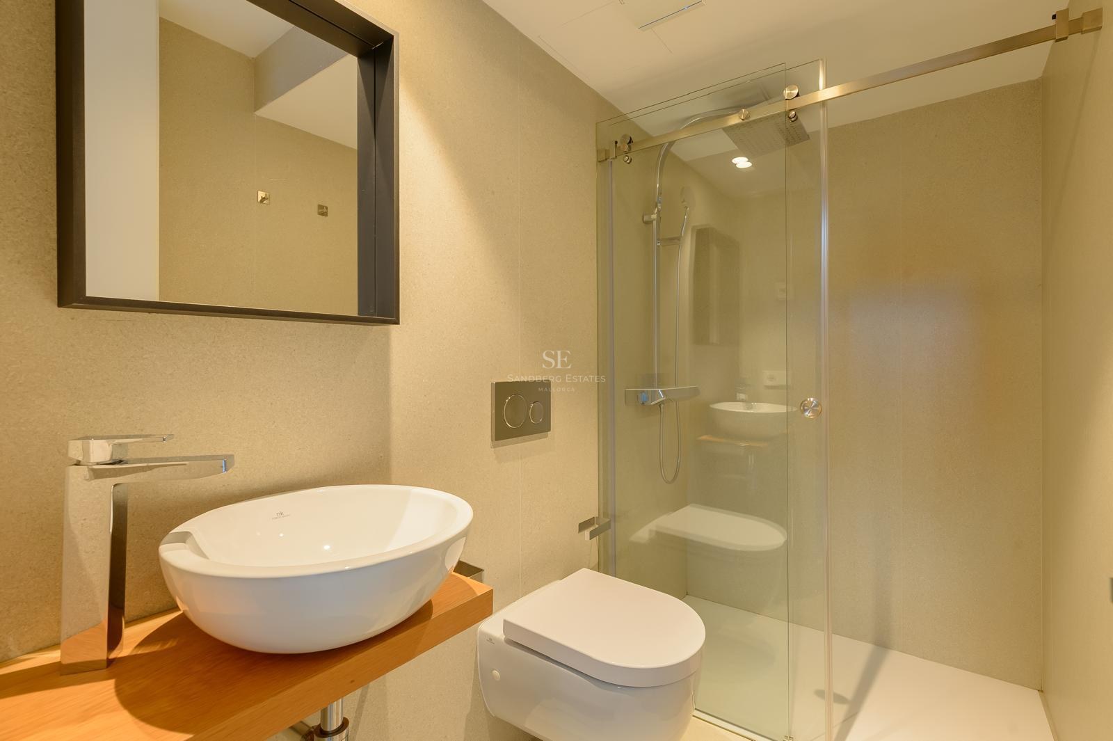 Baño contemporáneo con lavabo blanco sobre madera, inodoro suspendido y ducha de obra con mampara de cristal.