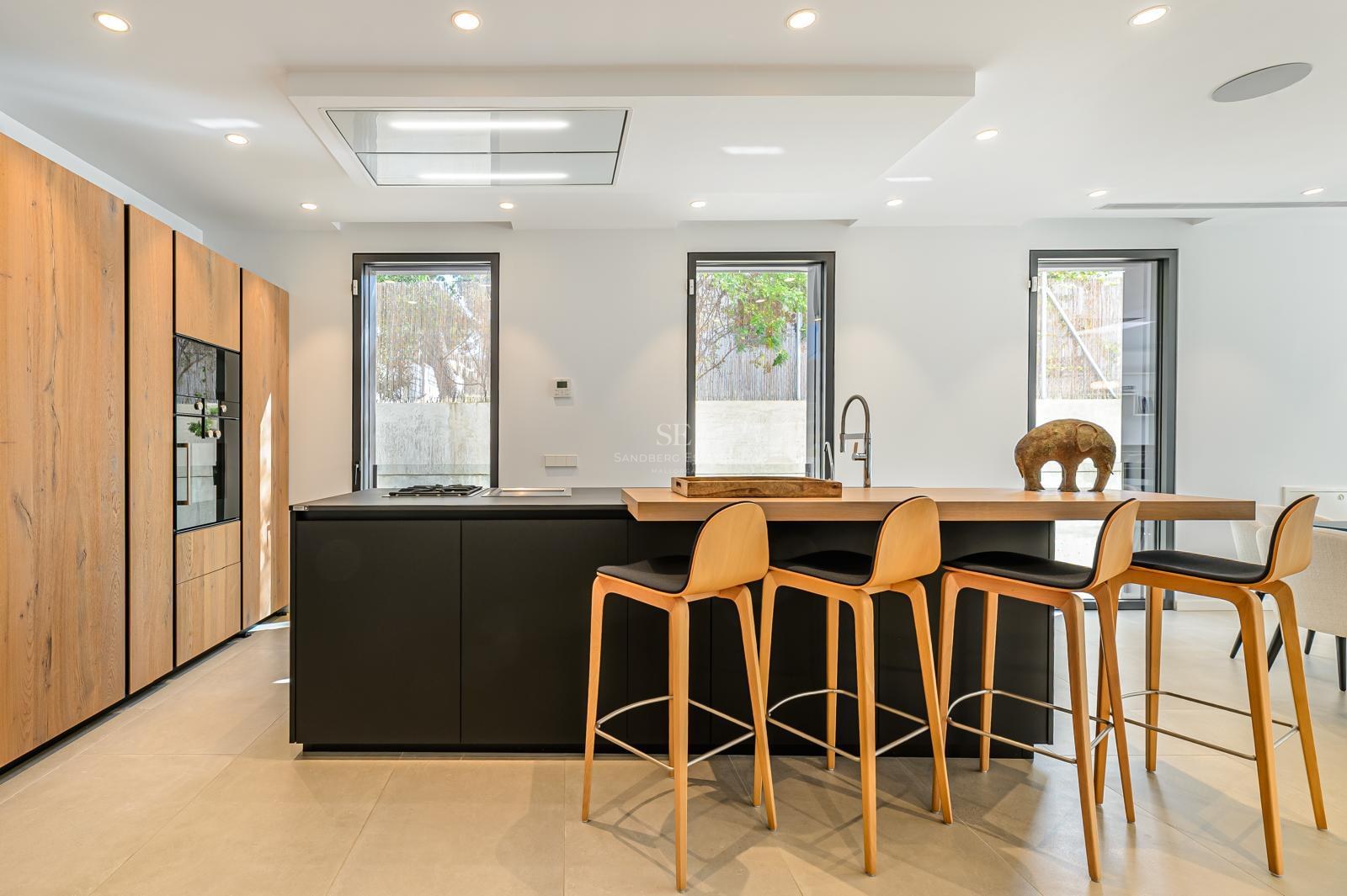 Cocina moderna con isla negra, barra de madera, cuatro taburetes y armarios de madera de suelo a techo.