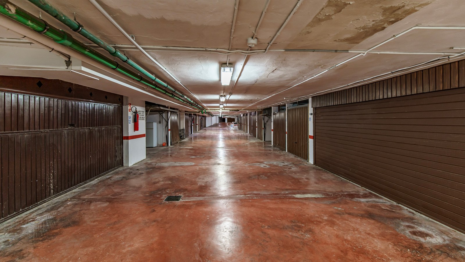 Underjordisk garagegång med rött betonggolv och bruna garageportar på båda sidor.