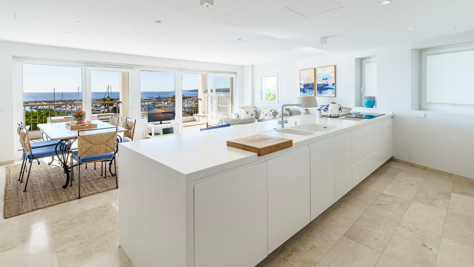 Minimalistisk vit köksö som leder till en matplats med panoramautsikt över marinan och havet.