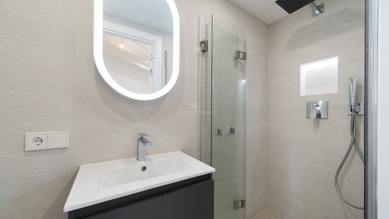 Modern bathroom vanity featuring a white sink, oval backlit LED mirror, and frameless glass shower enclosure.