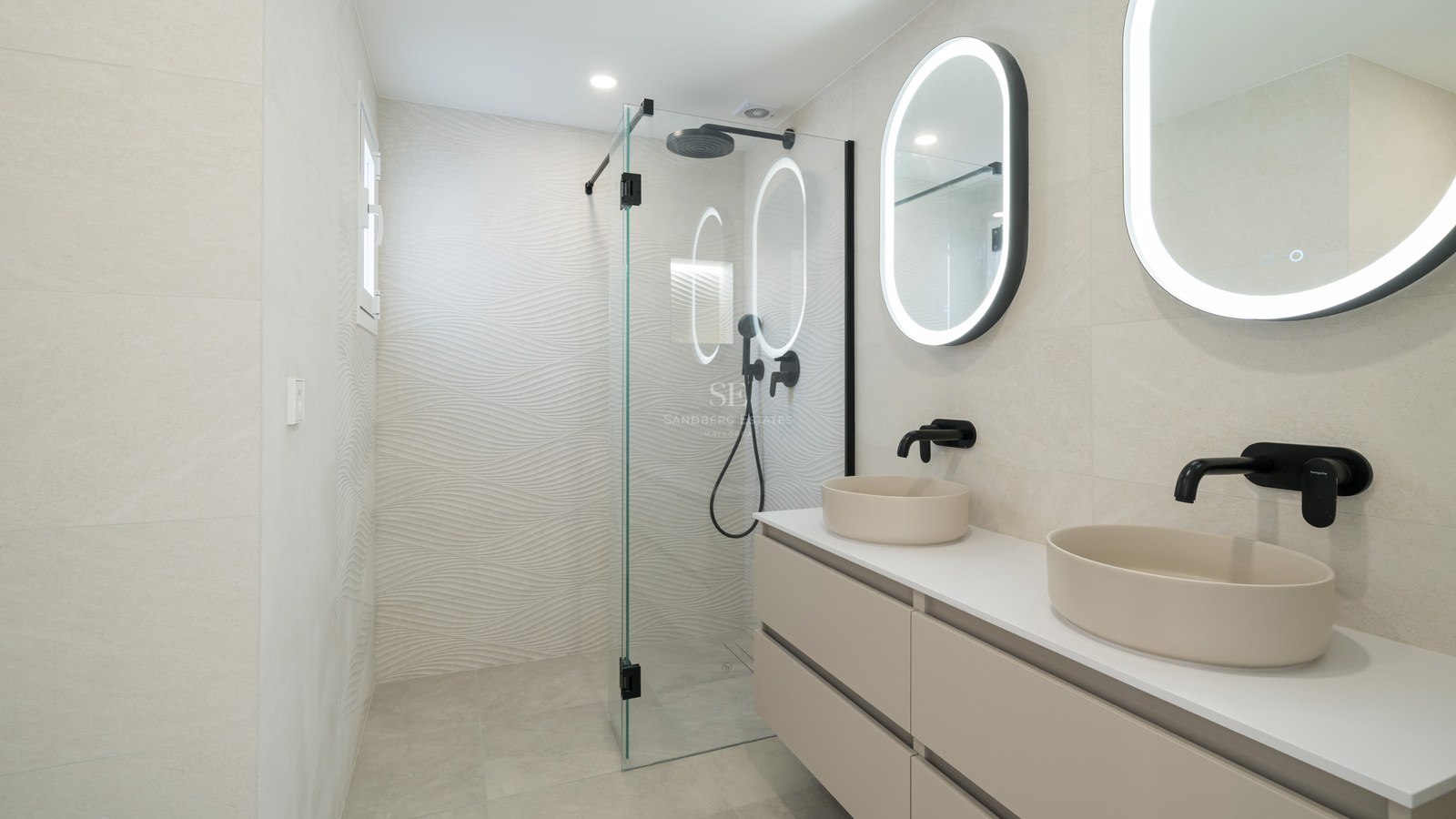 Minimalist bathroom featuring a walk-in glass shower, black faucets, and oval backlit mirrors over a floating vanity.