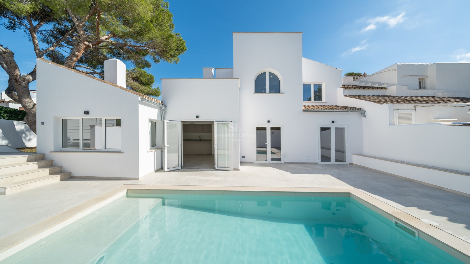 Turquoise swimming pool in front of a clean white modern Mediterranean villa under a clear blue sky.