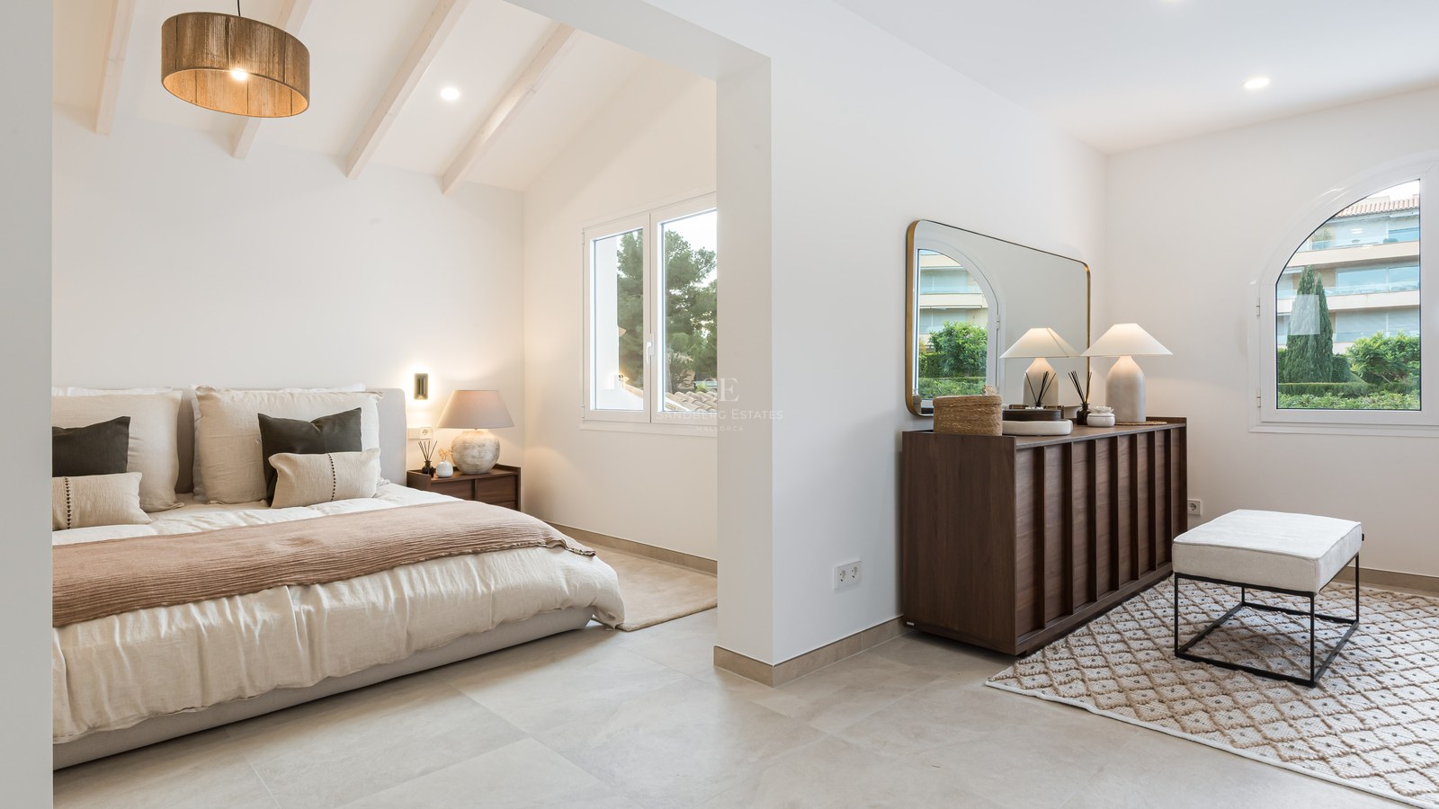 Modernt master bedroom med vita takbjälkar, stor säng, mörk träbyrå och naturligt ljus från fönster.