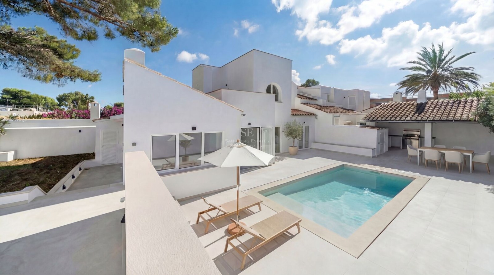 Modern vit villa med en rektangulär pool, solstolar och en utomhusmatplats under ett tegeltak.