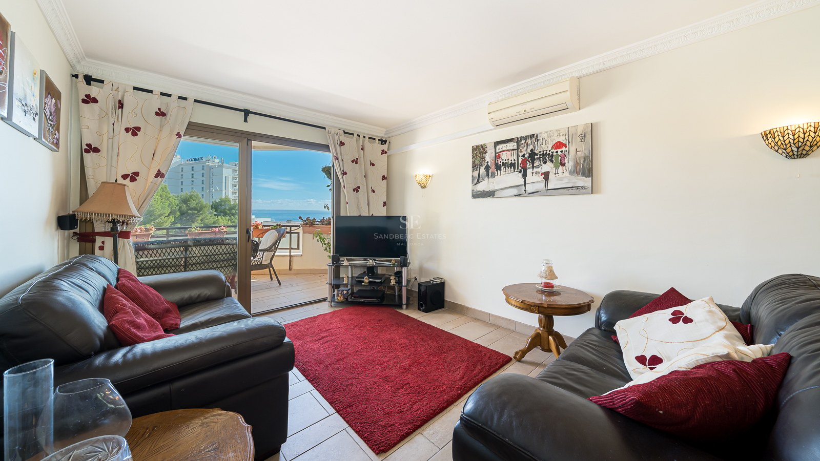 Living room with black leather sofas, a red rug, and a sliding door opening to a sea-view terrace.