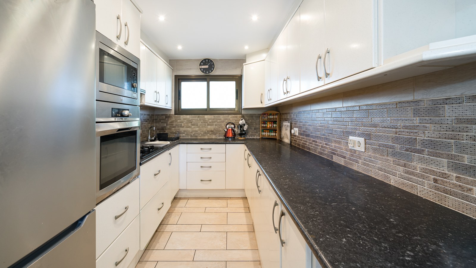 Galley kitchen featuring white cabinets, dark granite countertops, and built-in stainless steel appliances.