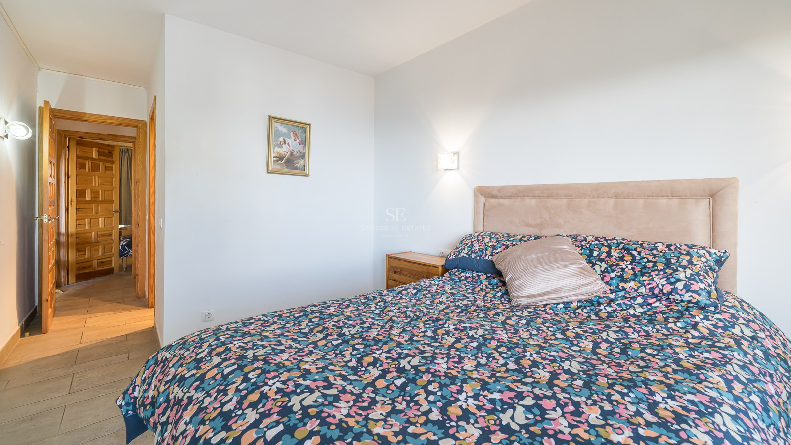 A bedroom featuring a large bed with a floral duvet, upholstered headboard, and rustic paneled wooden doors.