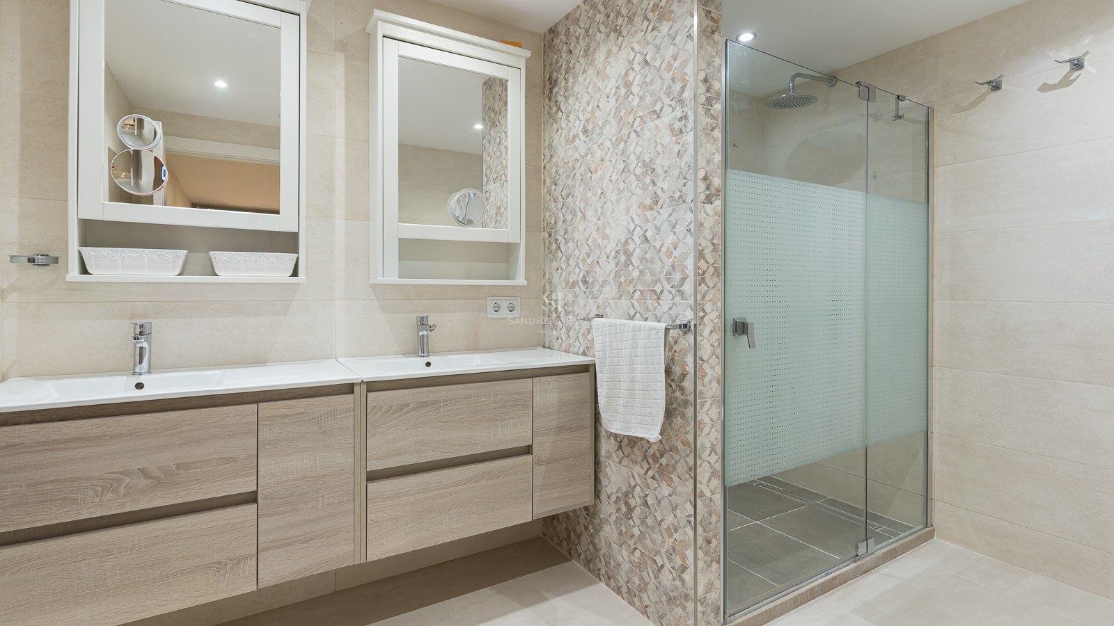 Bright master bathroom featuring a light wood double vanity, two mirrors, and a glass-enclosed walk-in shower.