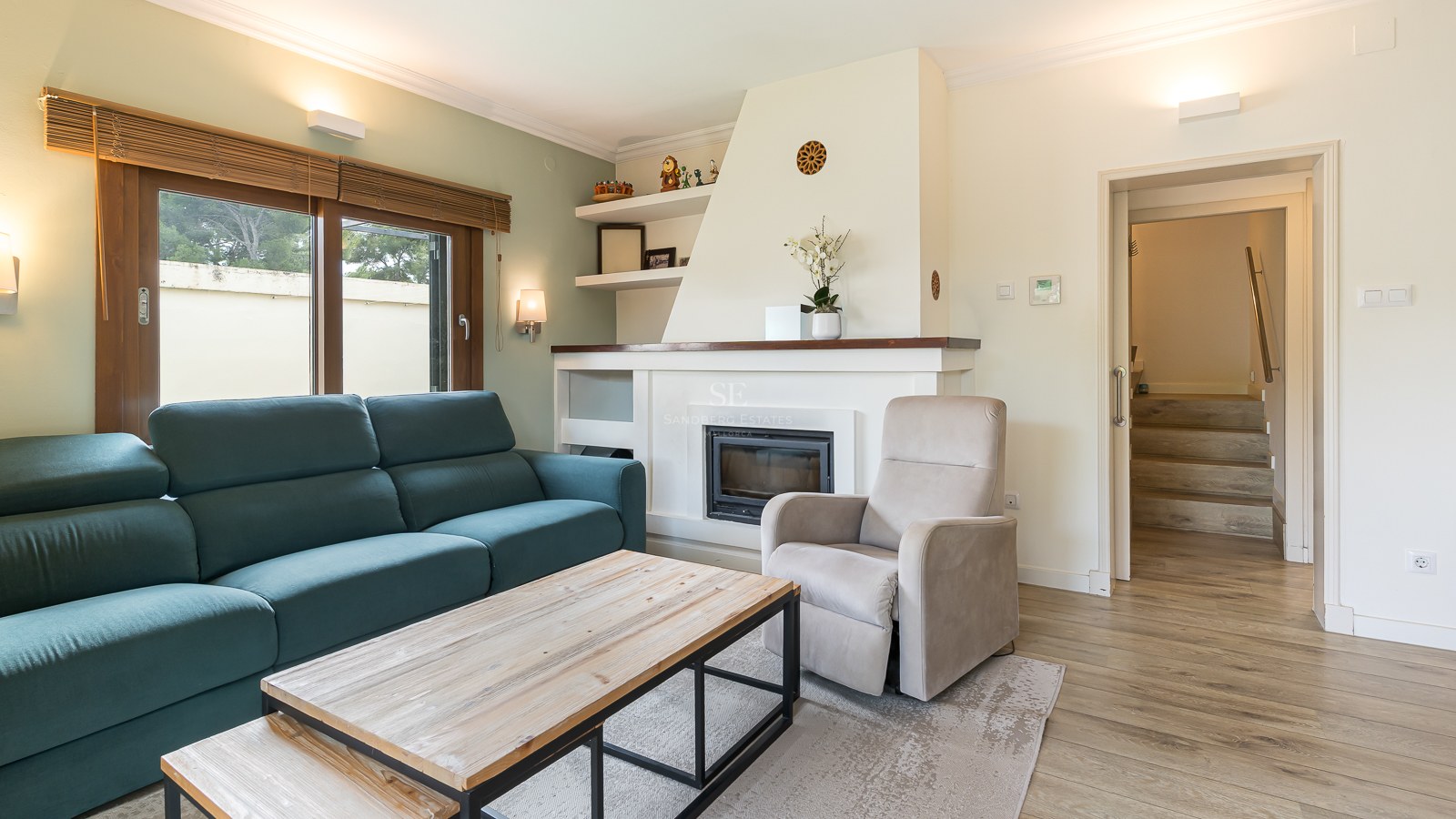 Modern living room with a teal sofa, white built-in fireplace, wooden coffee table, and beige armchair.