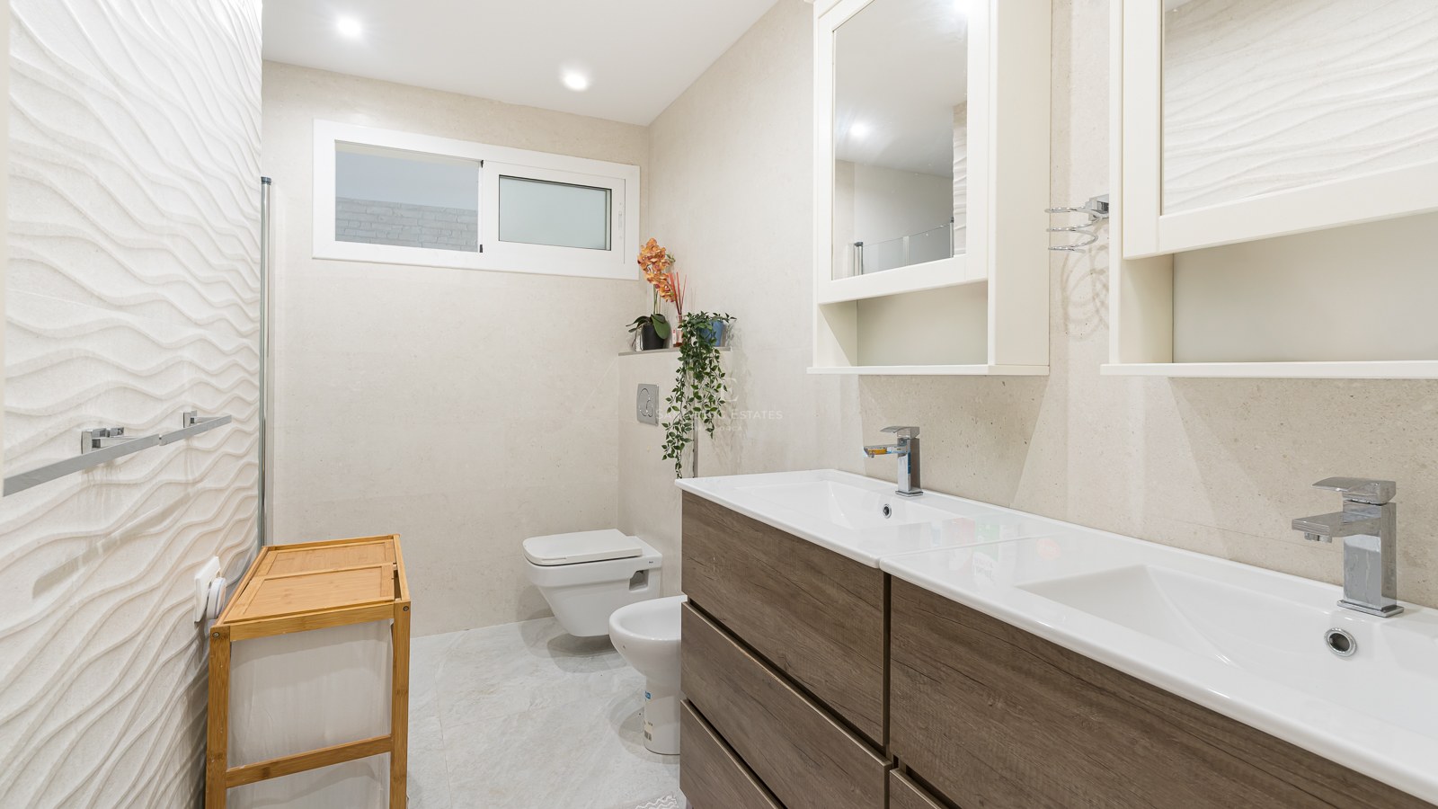 Modern bathroom with wood-finish double vanity, textured wall tiles, wall-hung toilet, and bidet.
