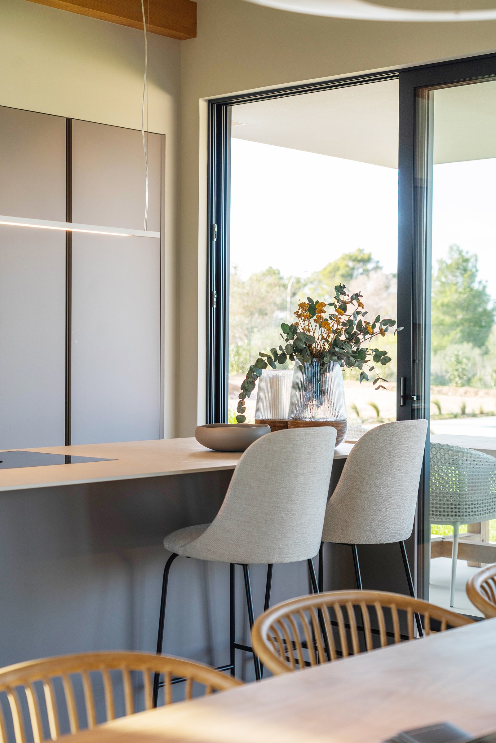 Modern kitchen island with grey bar stools next to a large glass door overlooking a garden.