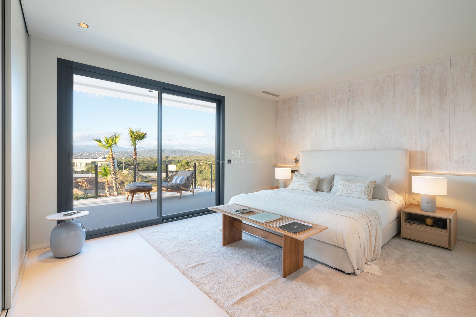 Luxury bedroom with white bed, wood accent wall, and glass door opening to a terrace with mountain views.