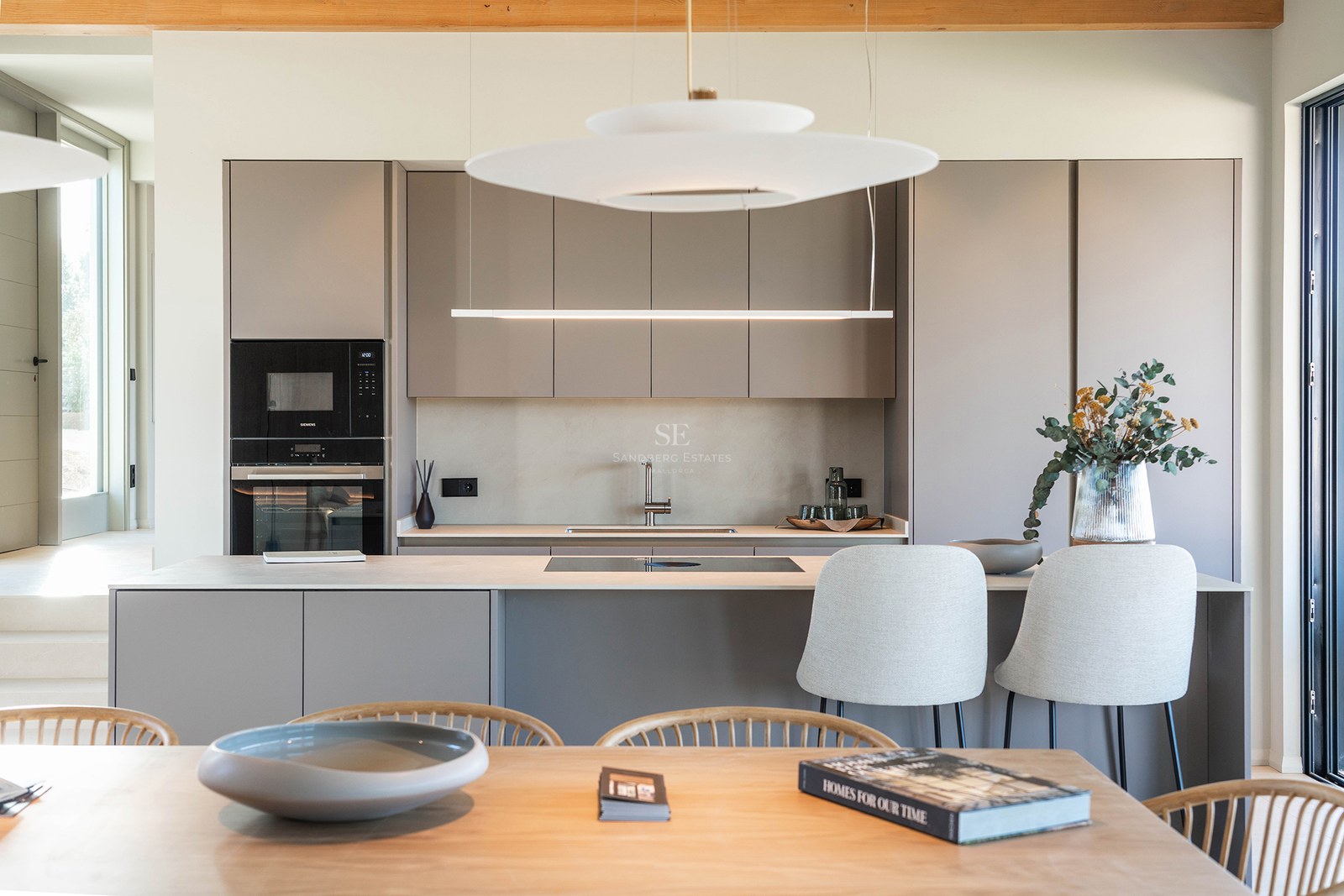 A contemporary kitchen featuring taupe handleless cabinets, a central island with stools, and elegant pendant lights.