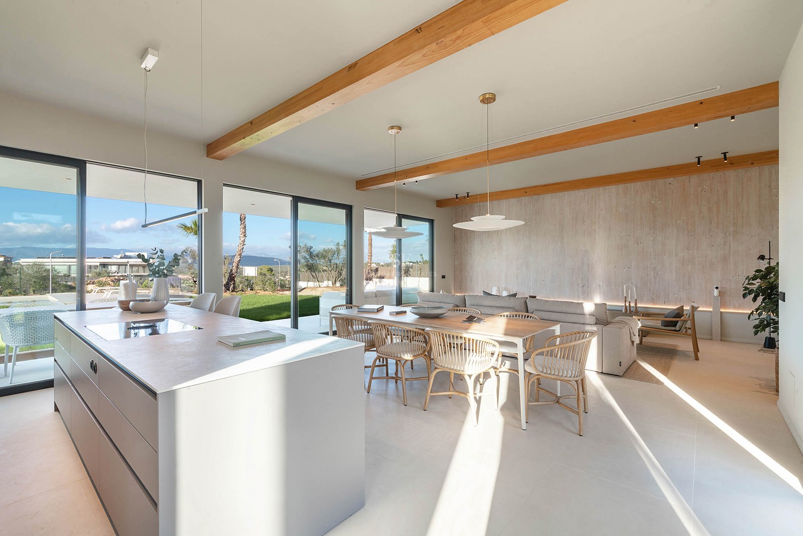 Spacious open-plan living room featuring wooden ceiling beams, kitchen island, dining area, and large glass doors to garden.