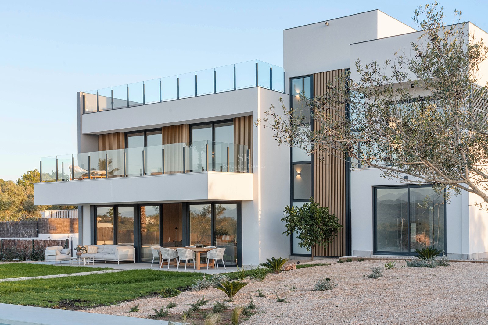 Two-story modern white villa with glass balconies, wooden slats, outdoor dining area, and a rooftop terrace.