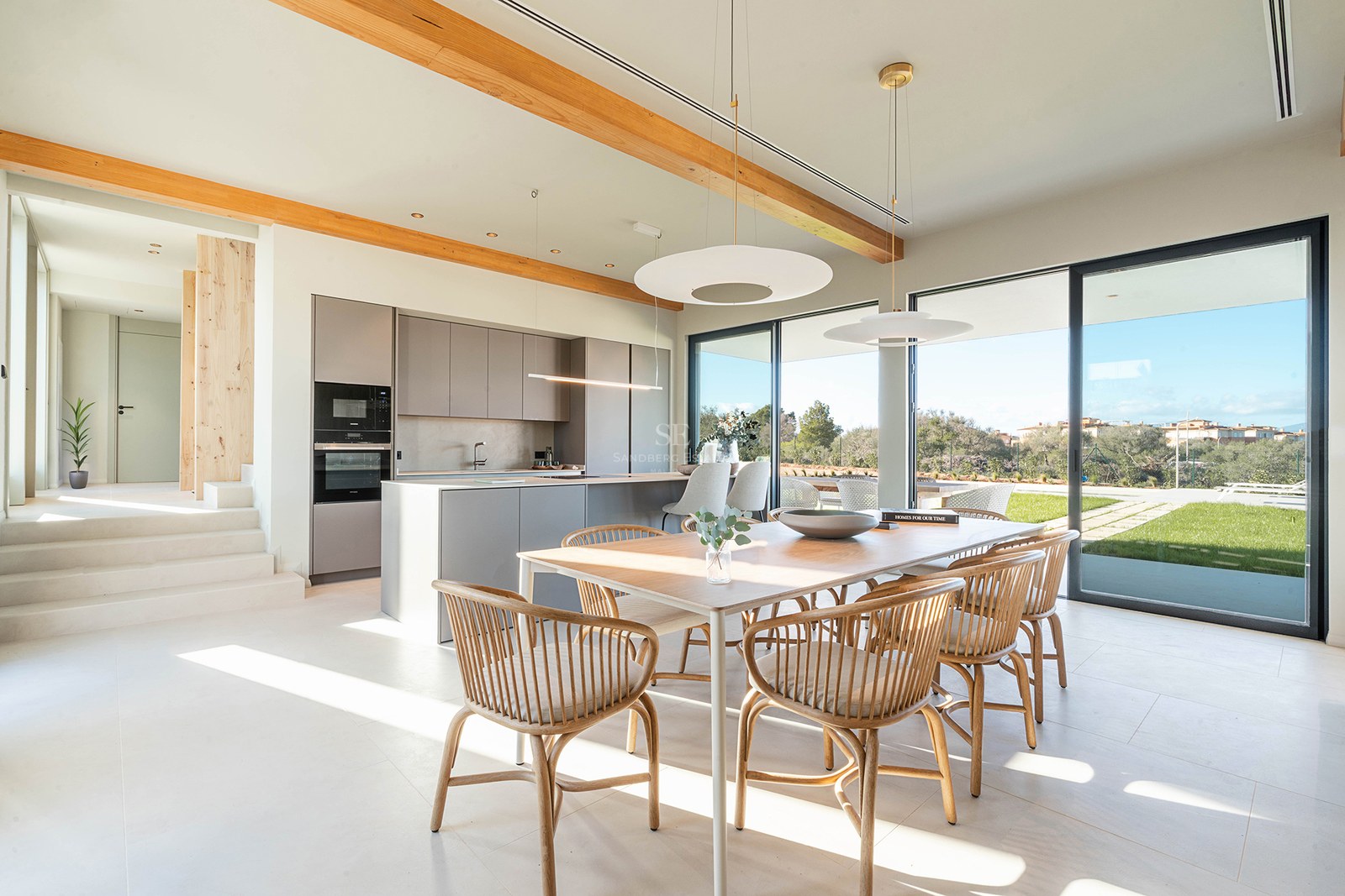 Bright dining room with wooden table and chairs next to a minimalist kitchen with large glass doors to garden.