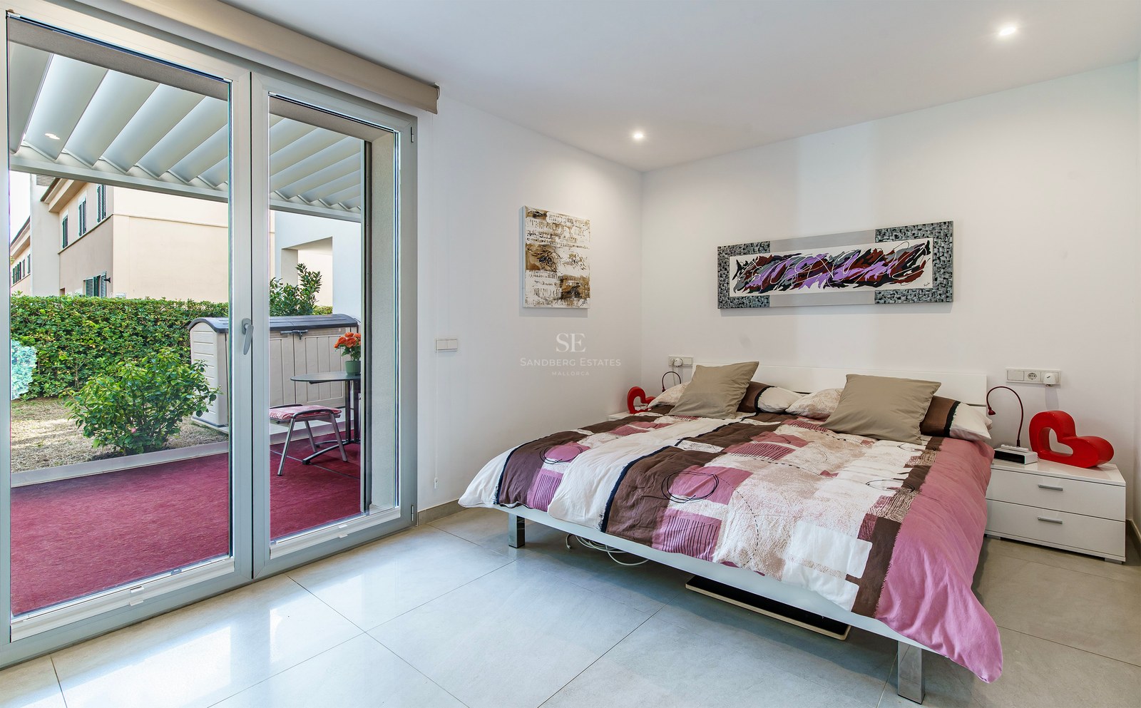 Chambre lumineuse avec un lit double, de l'art moderne et une grande porte vitrée coulissante ouvrant sur une terrasse.