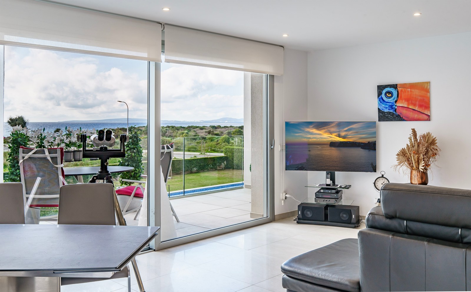 Salon lumineux avec grandes baies vitrées ouvrant sur terrasse avec vue mer, TV et canapé en cuir.