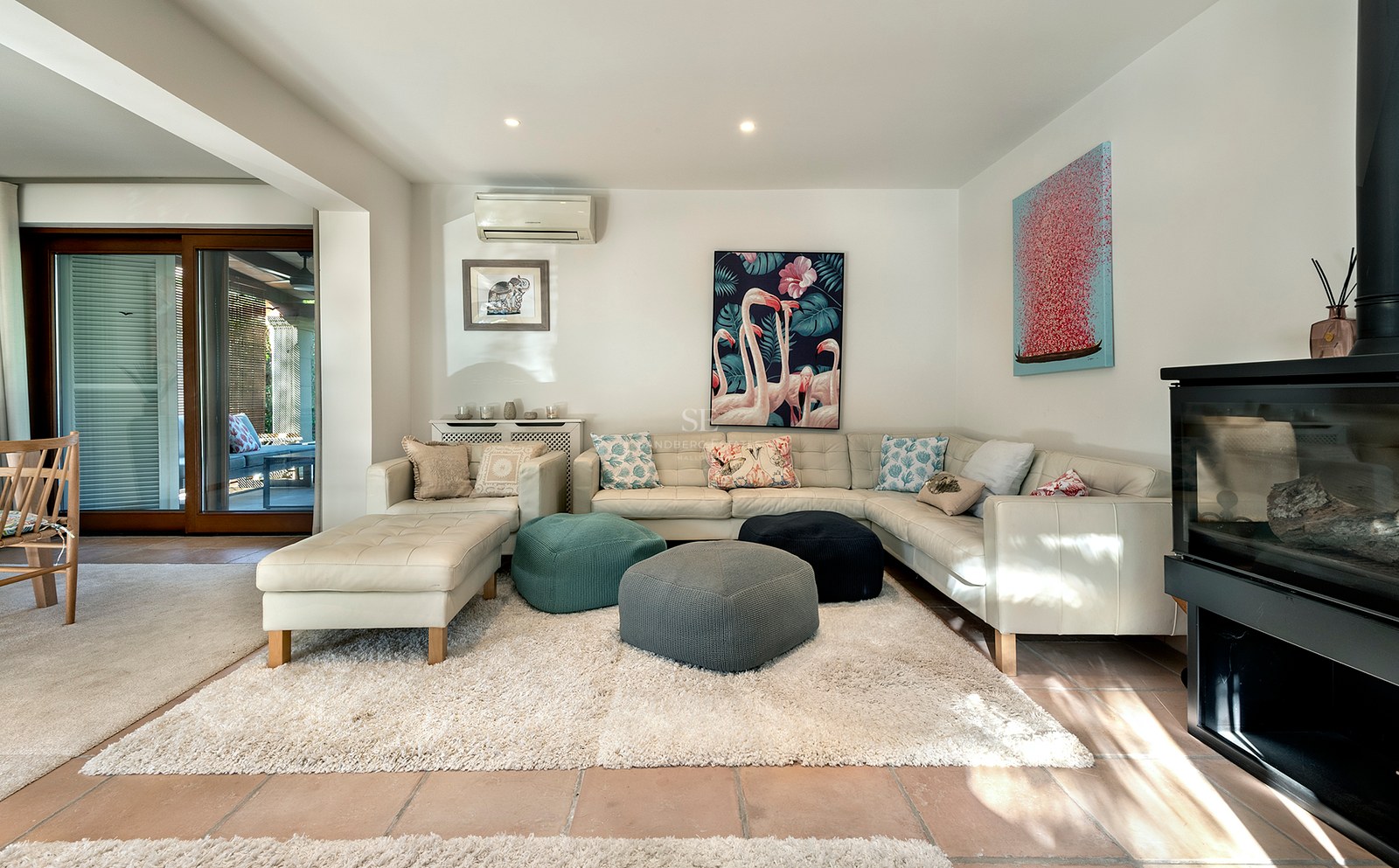Salón moderno con sofá de cuero blanco, pufs de colores, alfombra de pelo largo y chimenea de leña.