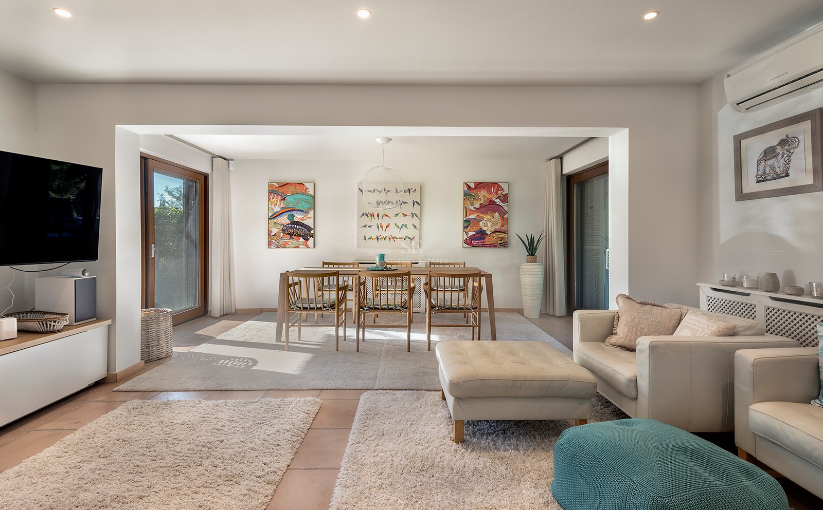 Sala luminosa de planta abierta con sofás de cuero crema, mesa de comedor de madera y arte de peces coloridos.