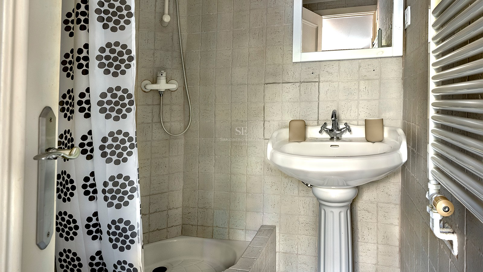 Baño pequeño con lavabo de pedestal blanco, paredes alicatadas y ducha con cortina de círculos.