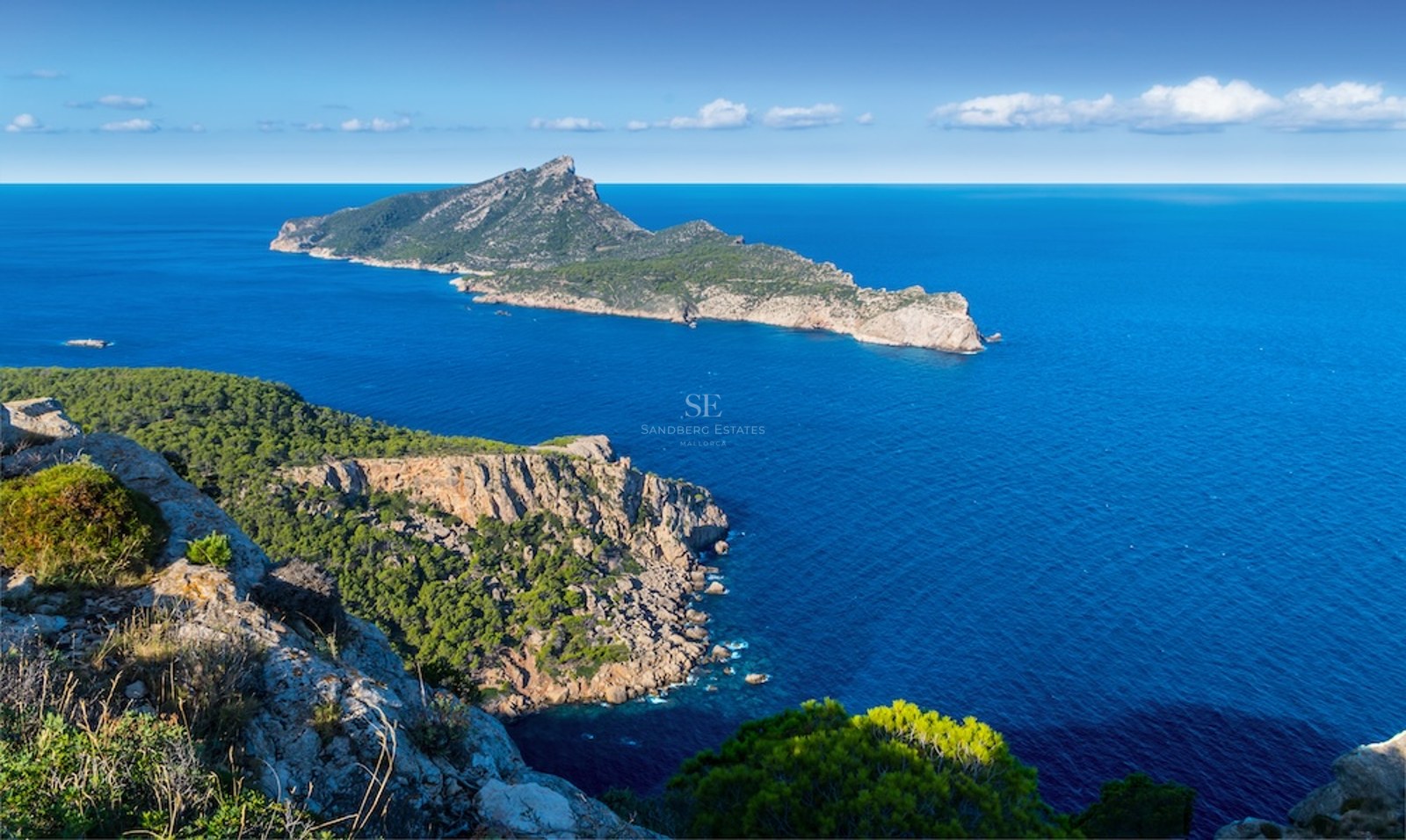 Vista elevada de la costa rocosa de Mallorca con la isla Dragonera sobre el mar Mediterráneo azul profundo.
