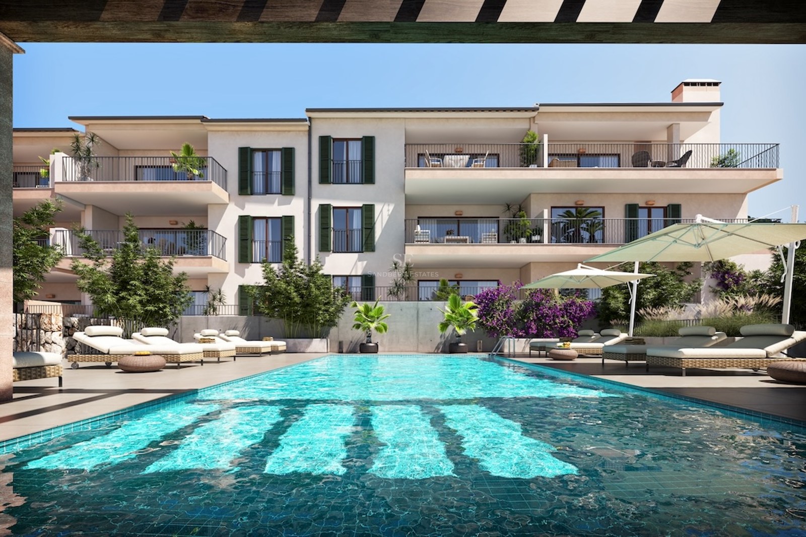 Outdoor swimming pool with sun loungers in front of a modern Mediterranean building with balconies and green shutters.