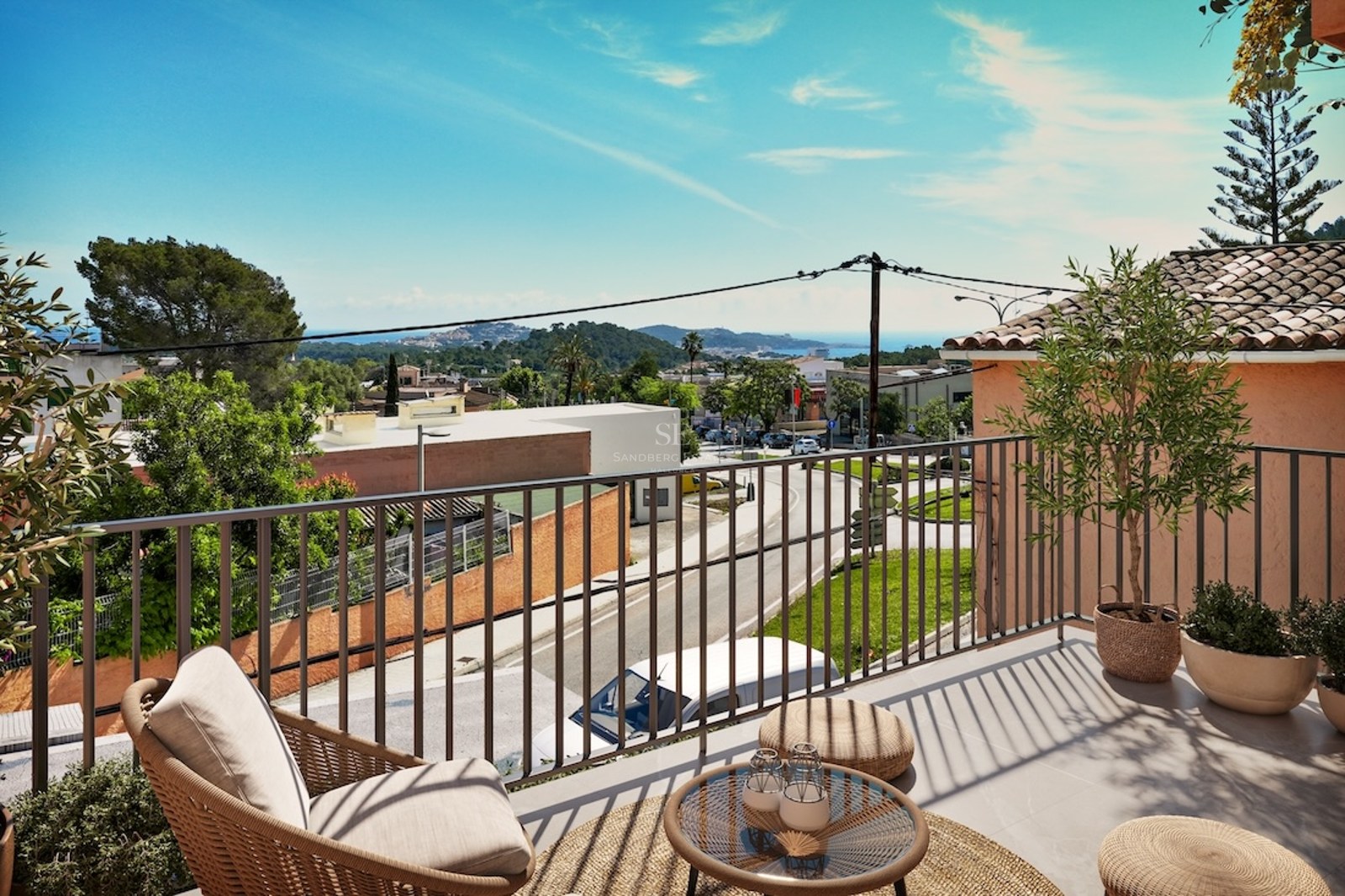 A sunny elevated terrace with a wicker armchair and small table overlooking a coastal town and the sea.