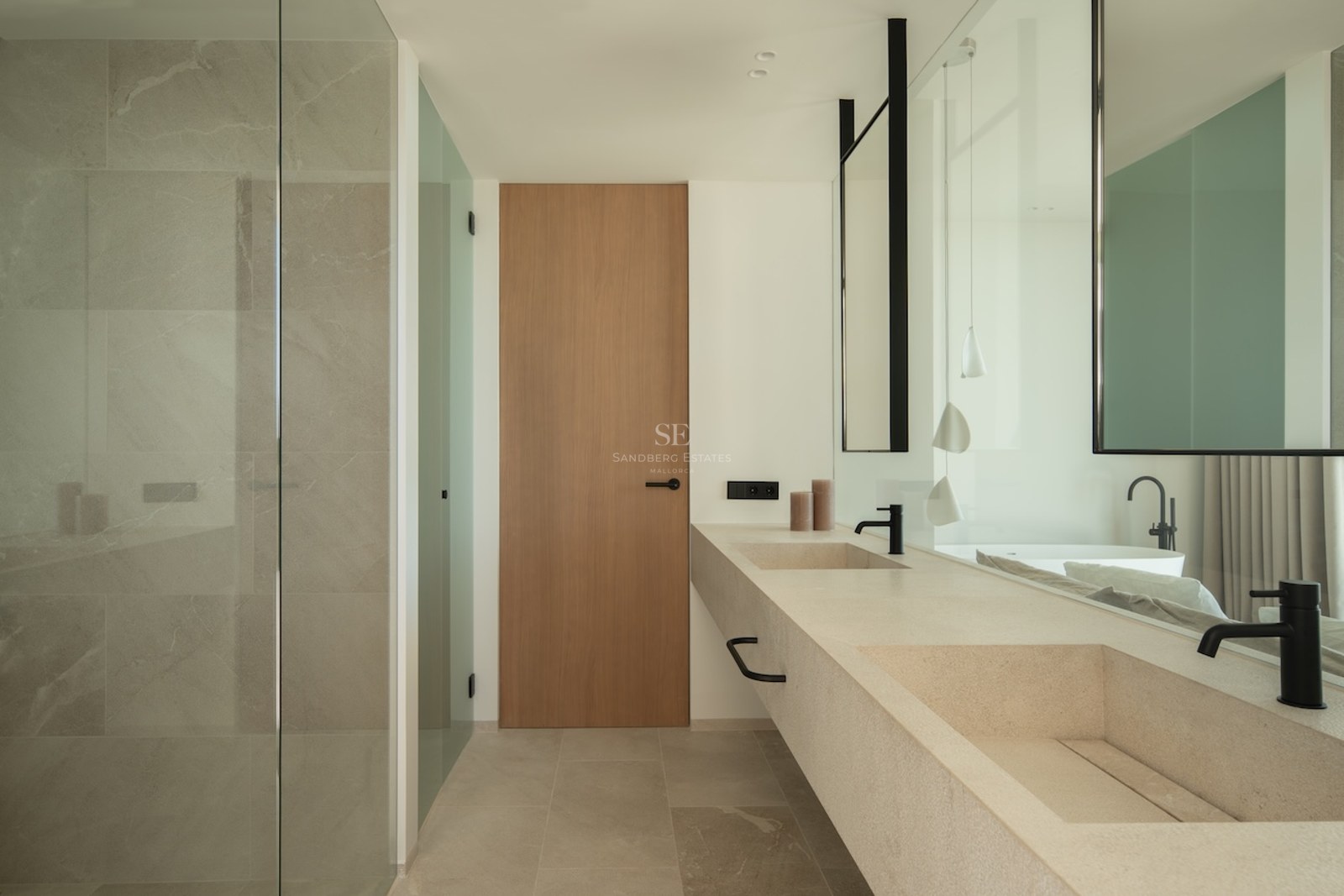 Minimalist bathroom featuring a long floating stone vanity with double sinks, light wood door, and glass shower.