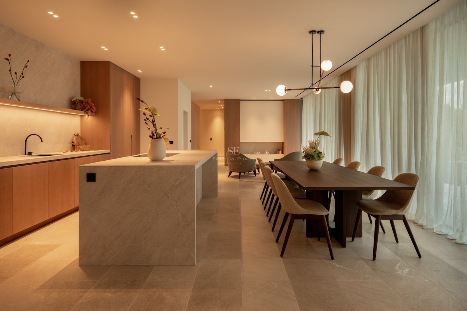 A contemporary open-plan dining room and kitchen featuring a marble island, dark wood table, and warm designer lighting.