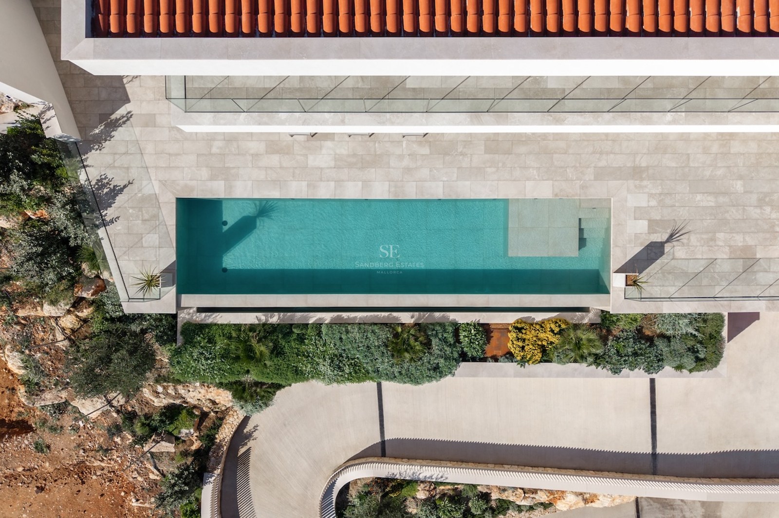Bird's eye view of a turquoise swimming pool, stone terrace, terracotta roof, and lush Mediterranean landscaping.
