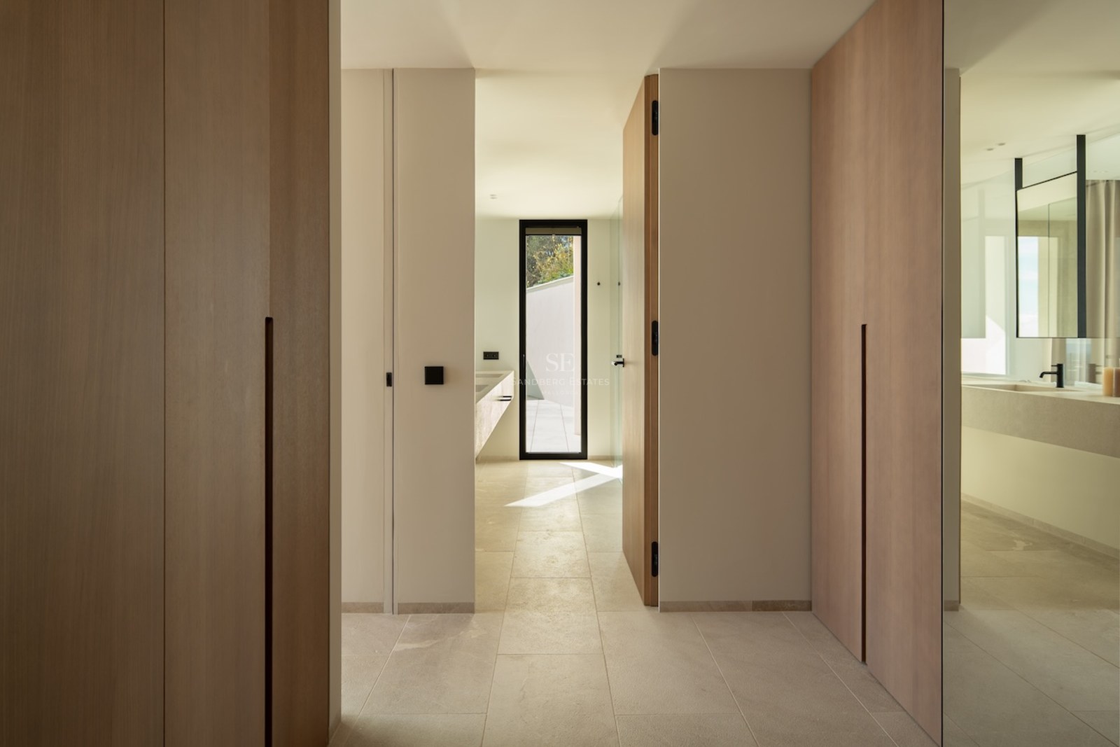 Hallway with floor-to-ceiling light wood wardrobes leading to a bright bathroom.