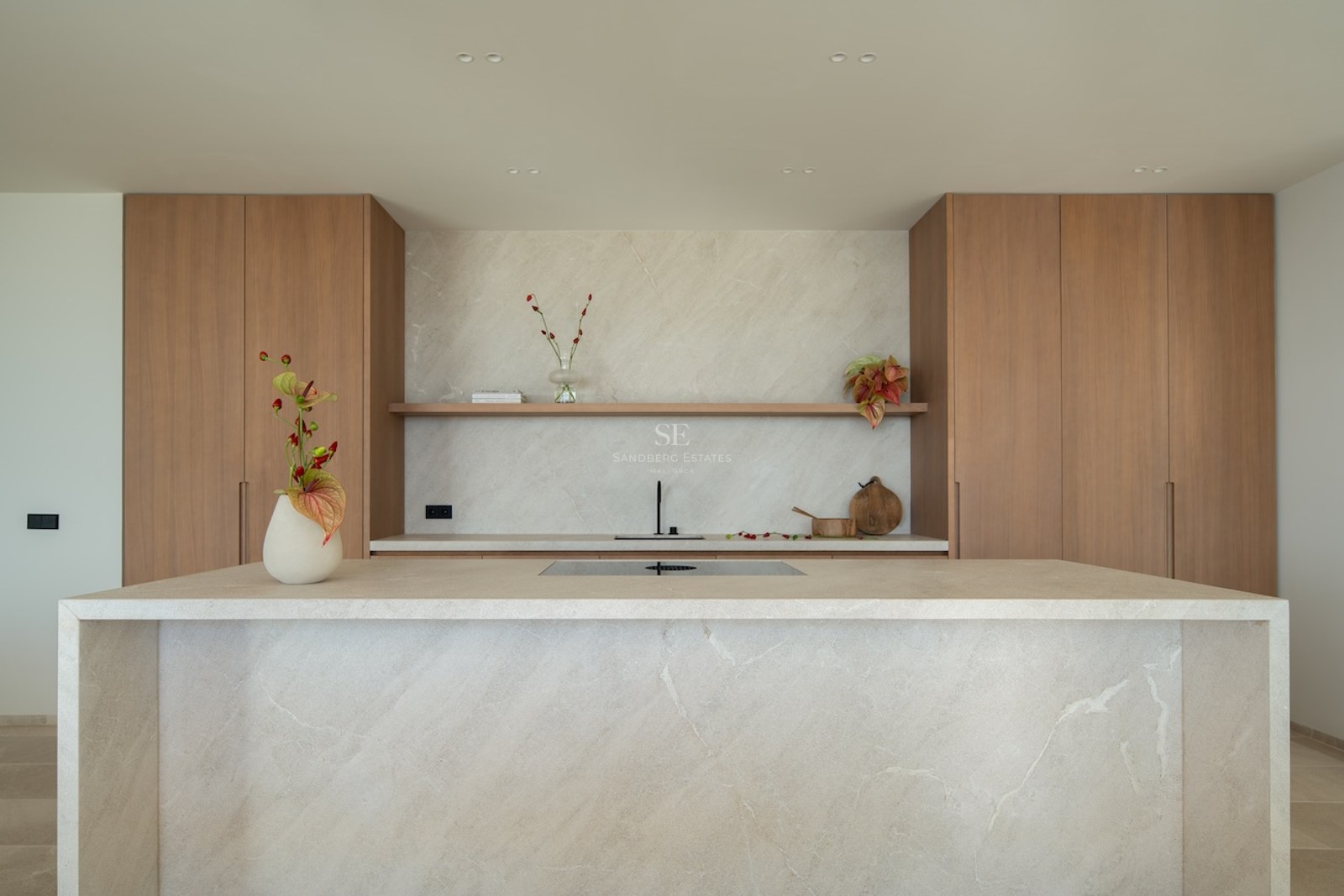 Modern kitchen featuring a large beige stone island, natural wood cabinets, and a matching stone backsplash.