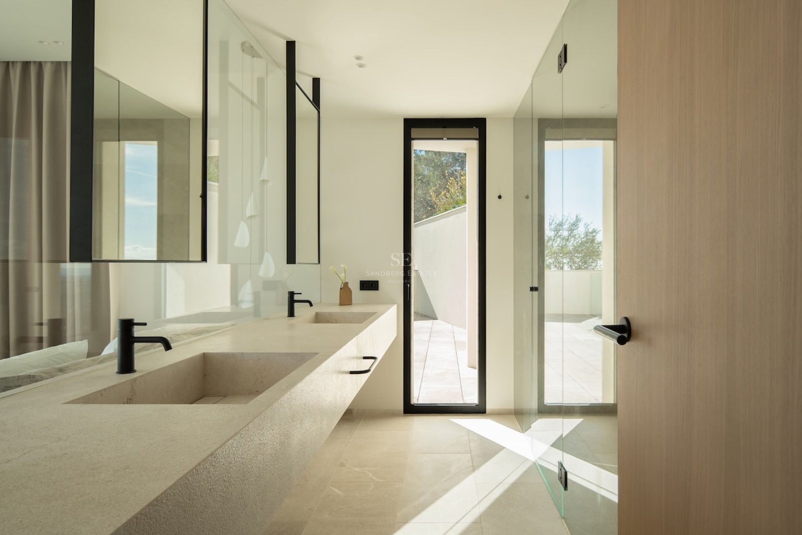 Modern bathroom featuring a long stone double vanity with black faucets, large mirrors, and natural light from a window.