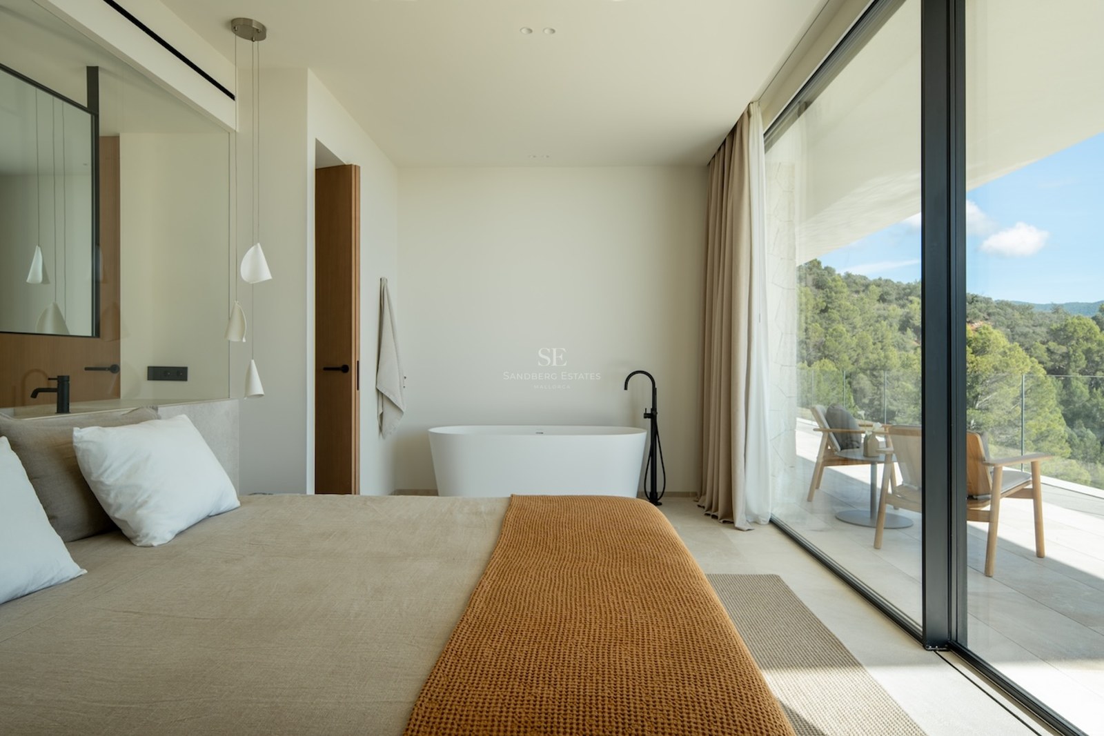 Luxury bedroom with a freestanding bathtub next to large glass doors overlooking a forest and private terrace.