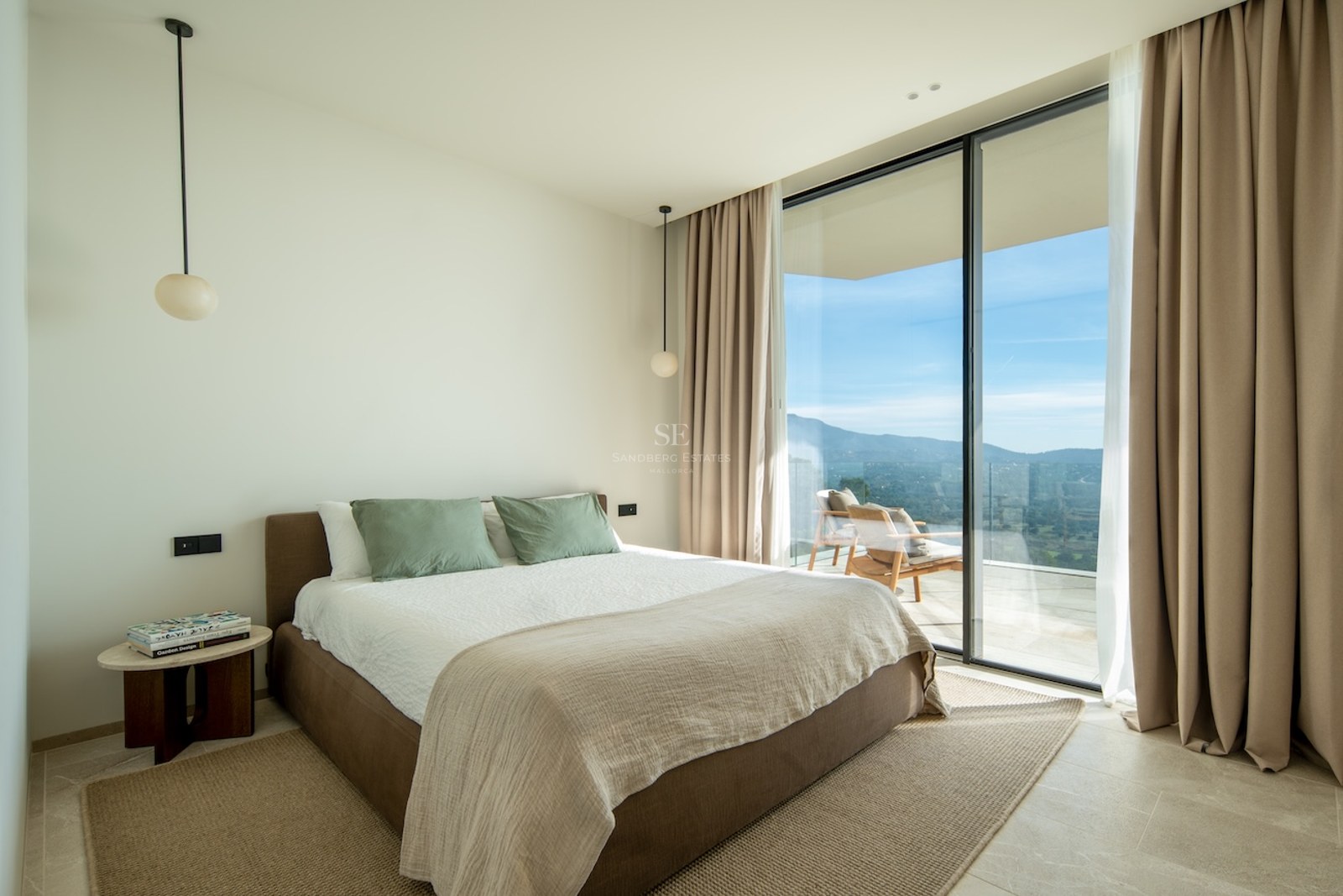 Modern bedroom with floor-to-ceiling windows leading to a terrace overlooking mountains.