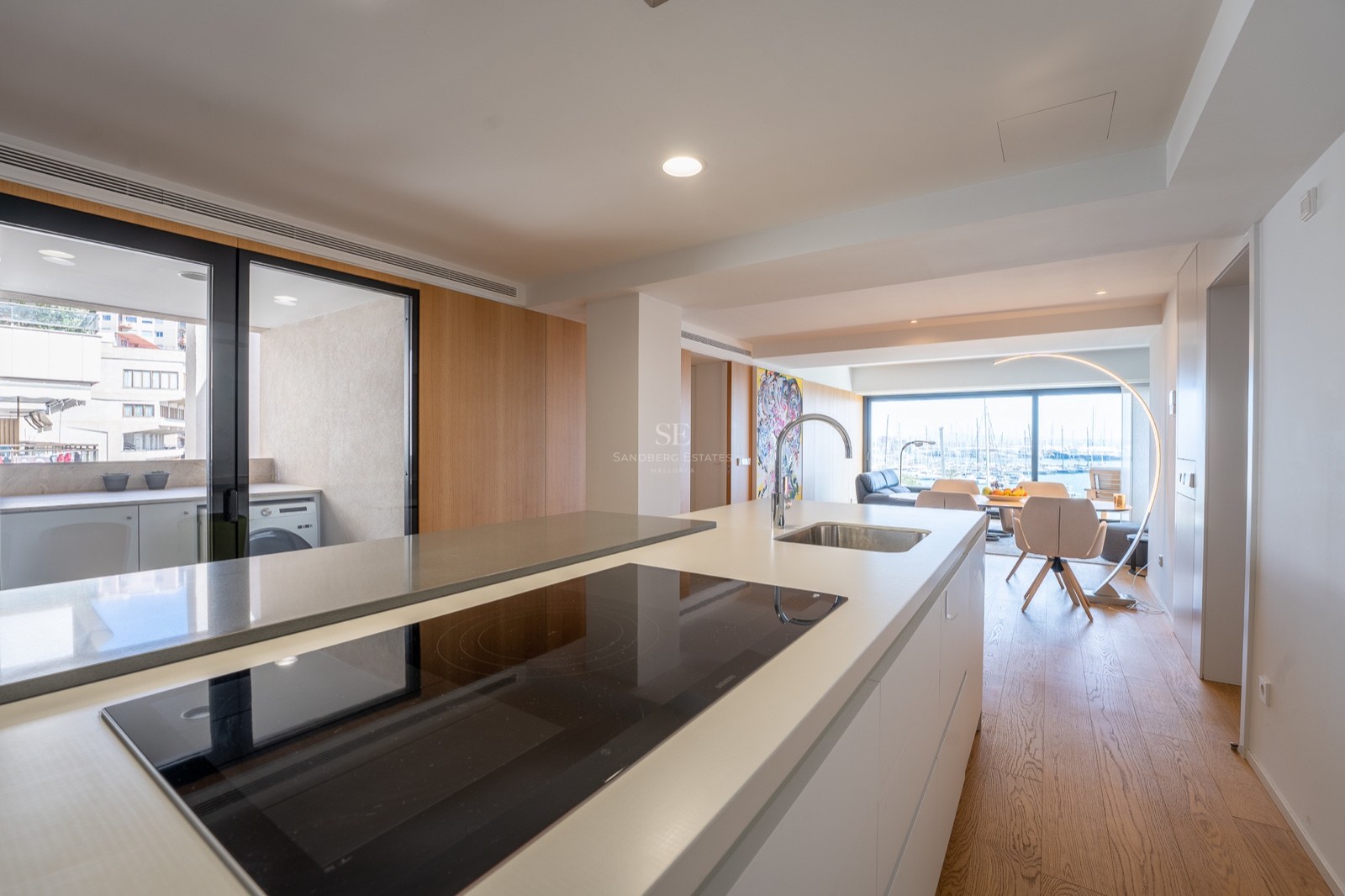 Îlot de cuisine avec plaque à induction et évier, ouvrant sur une salle à manger et le port en arrière-plan.