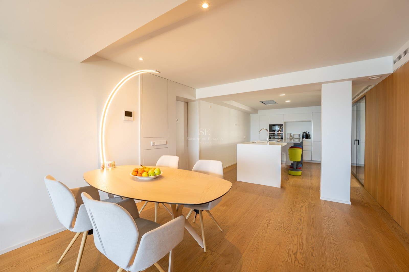 Salle à manger minimaliste avec table en bois clair, chaises grises et lampadaire arqué original.