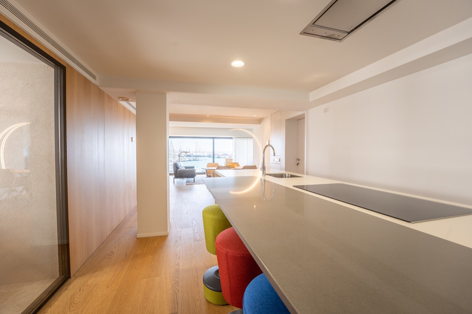 Îlot de cuisine avec tabourets colorés menant à un salon lumineux avec vue sur le port.
