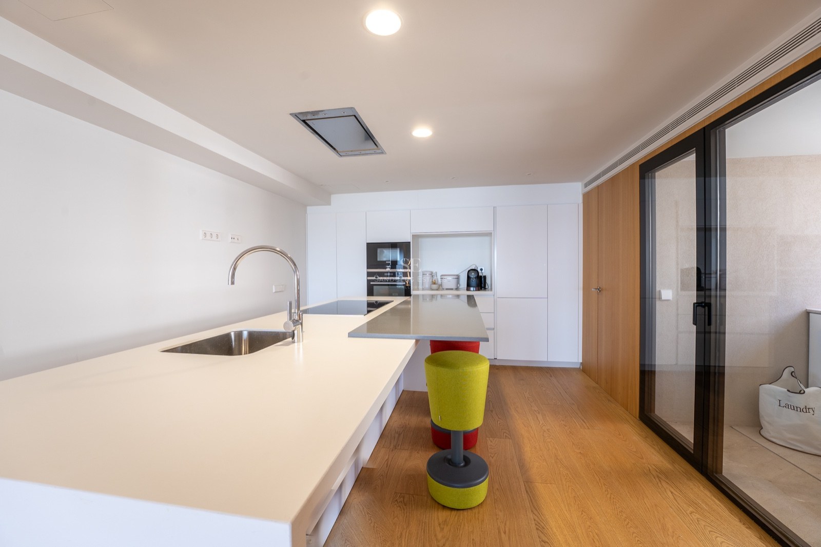 Intérieur de cuisine moderne avec un grand îlot blanc, un évier, du parquet et des appareils encastrés.