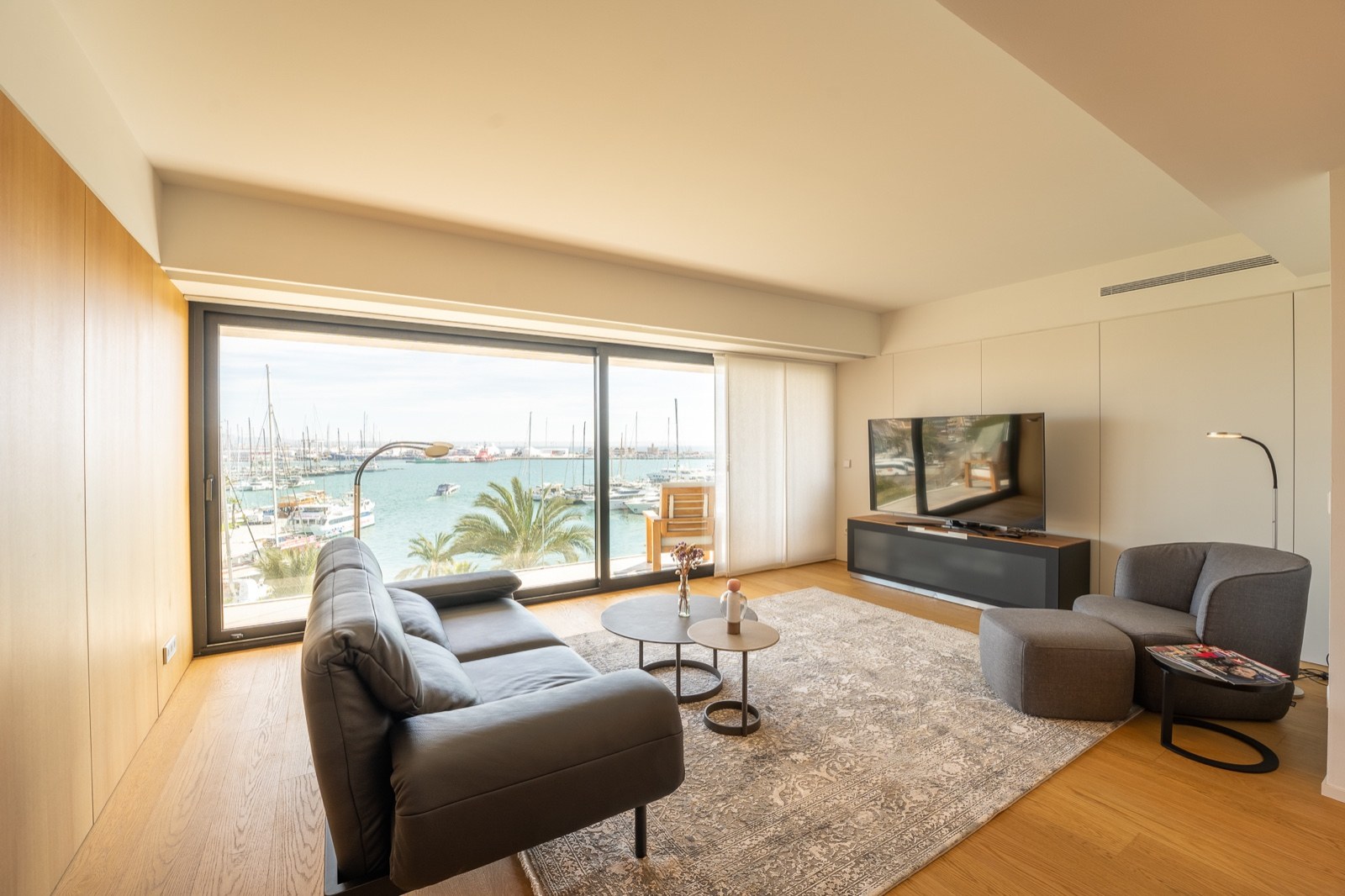 Salon contemporain avec canapé en cuir et grandes baies vitrées donnant sur un port avec des bateaux.