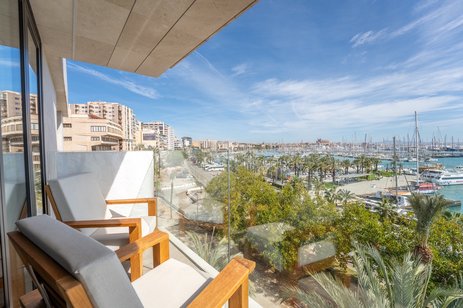 Balcon moderne avec fauteuils en bois et garde-corps en verre offrant une vue panoramique sur un port de plaisance.