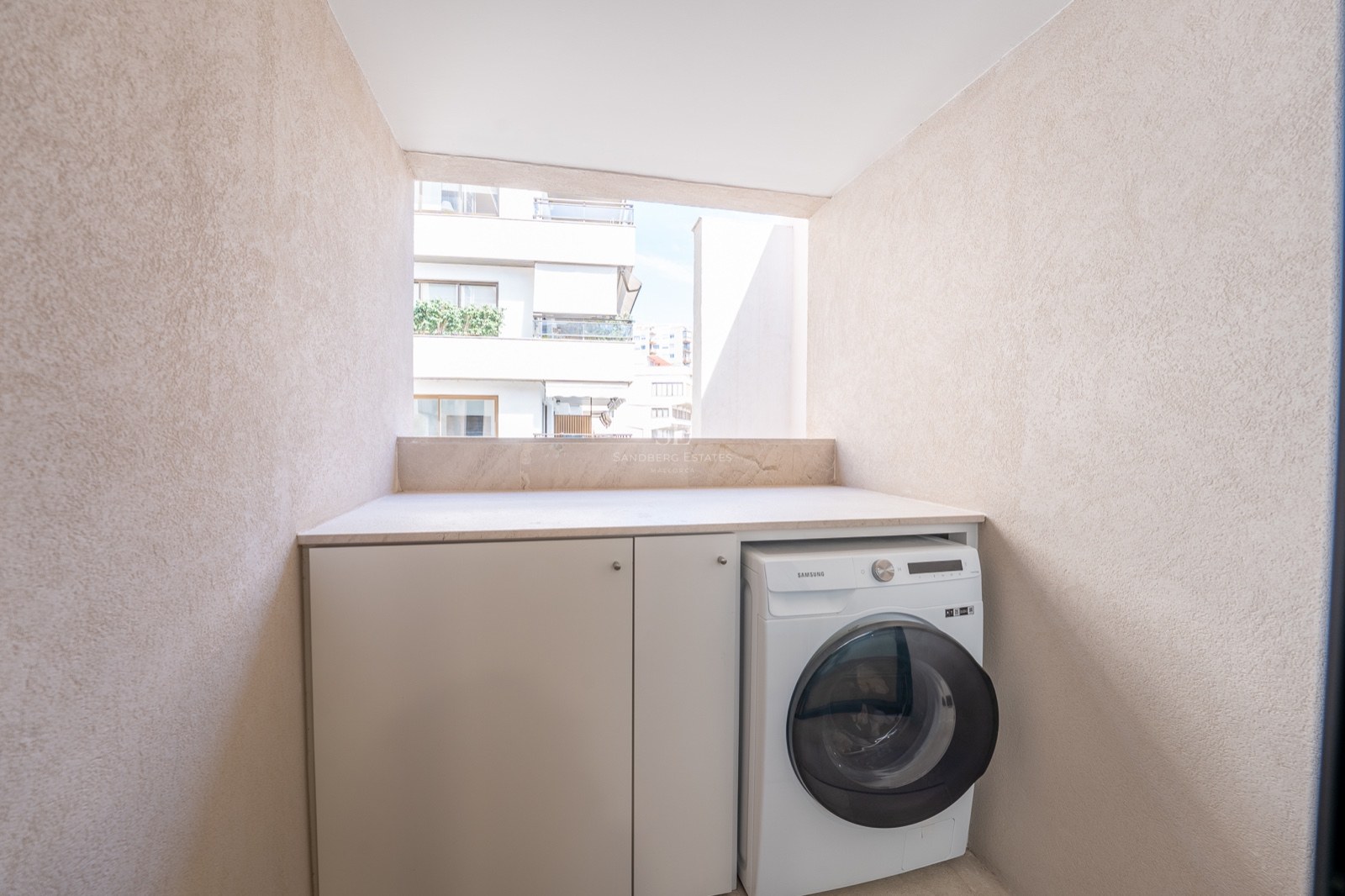 Lave-linge et placards blancs encastrés dans un coin de balcon aux murs beiges texturés.