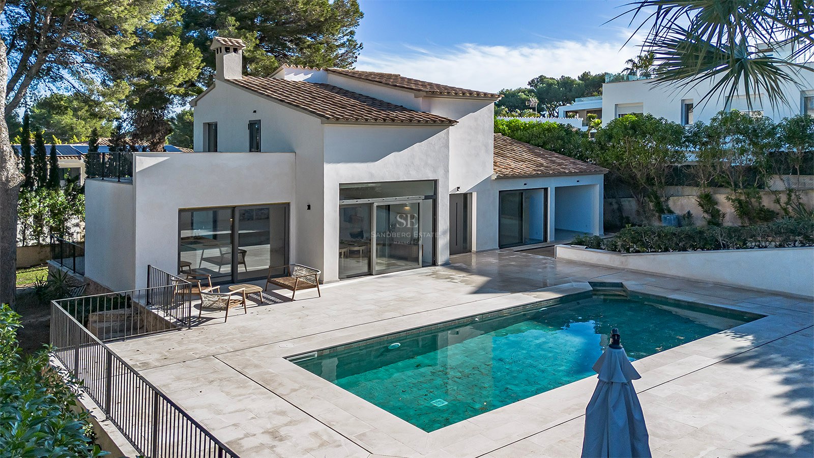 Villa blanca de estilo mediterráneo con una piscina rectangular azul y una amplia terraza de piedra bajo el sol.
