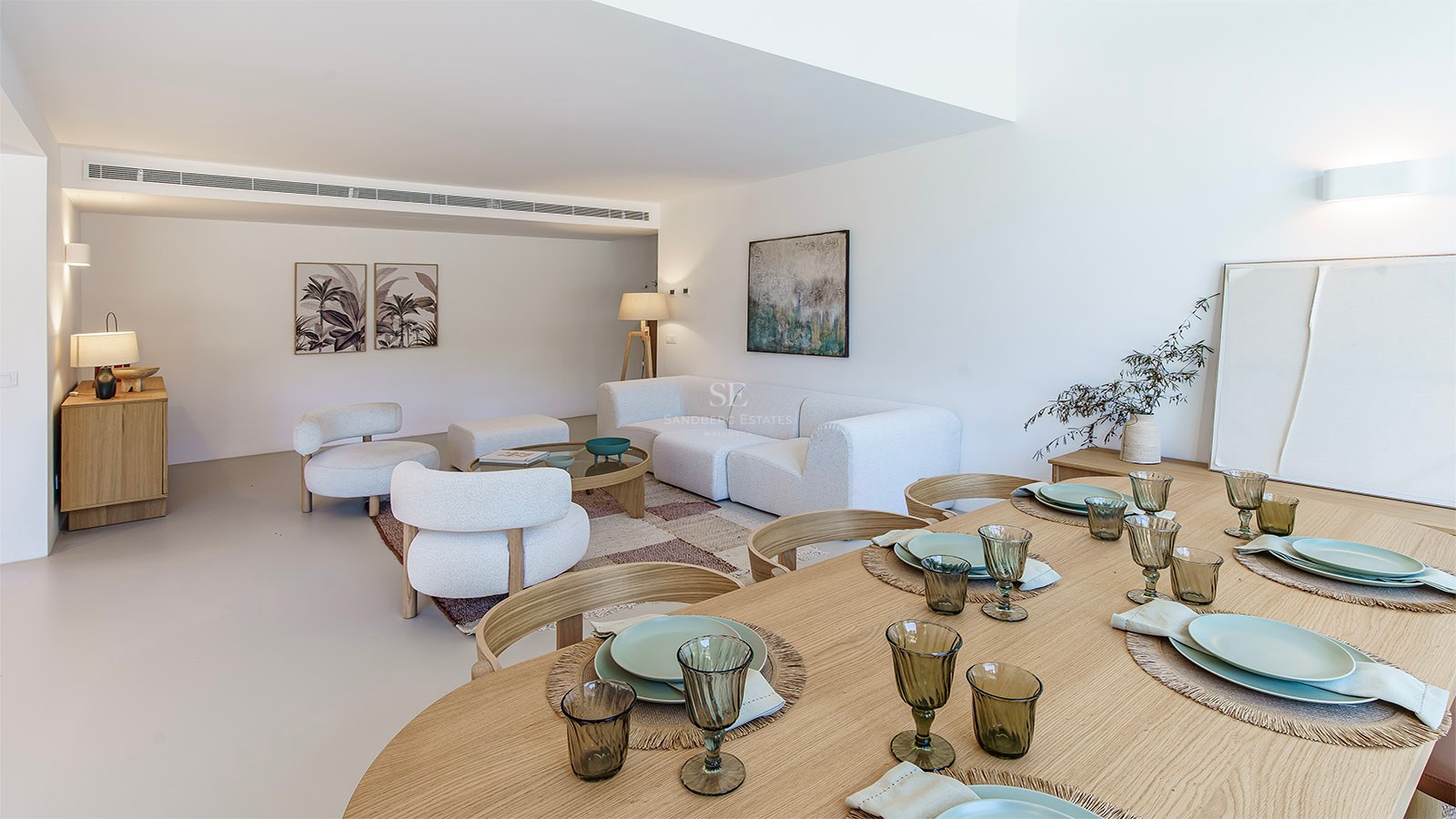 Amplio salón-comedor con sofás de tela bouclé blanca, mesa de comedor de madera y decoración minimalista.