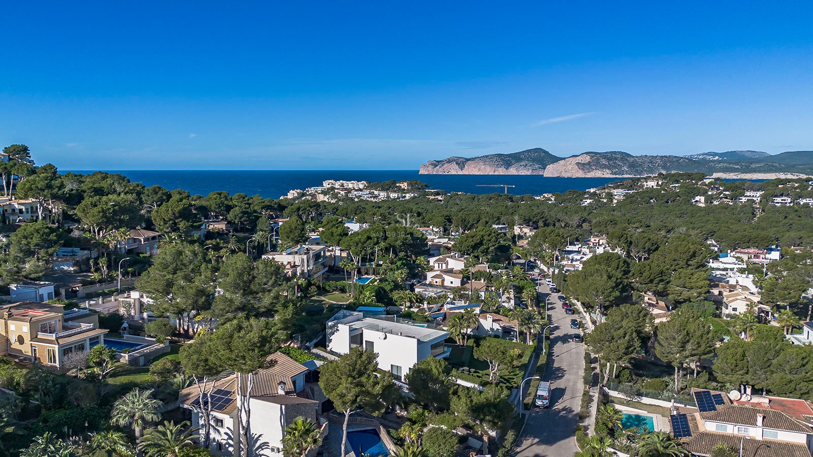 Vista de dron de un vecindario costero con casas de lujo, pinos y el mar Mediterráneo al fondo.