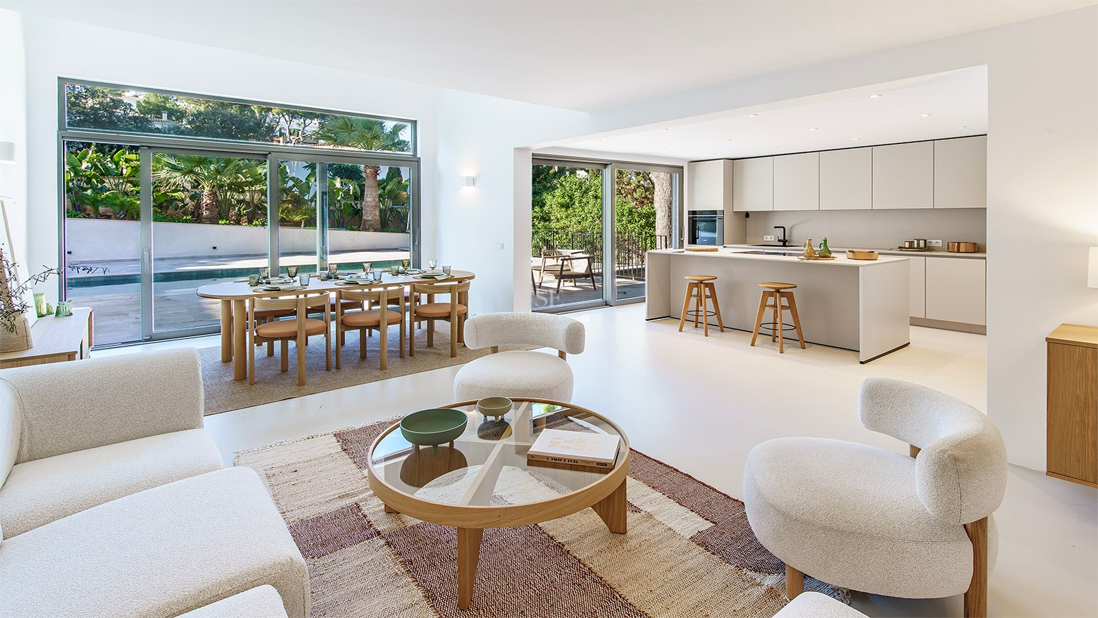 Amplio salón de concepto abierto con sofás blancos, comedor de madera y cocina moderna con vistas a la piscina.