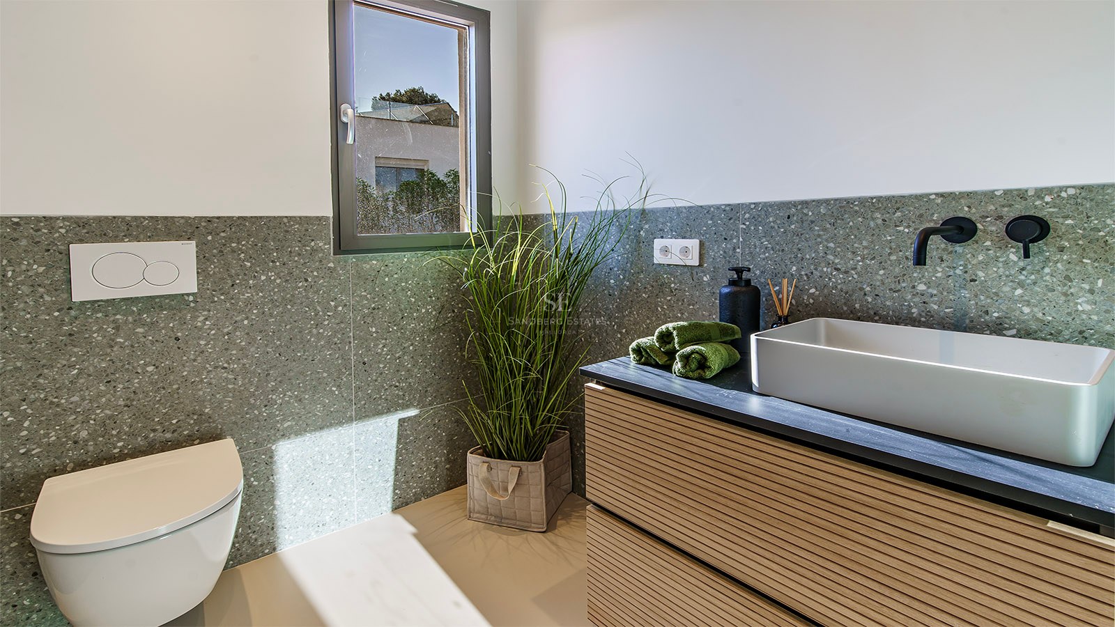 Baño minimalista con lavabo de sobreponer, grifo negro, inodoro suspendido y paredes de terrazo verde.